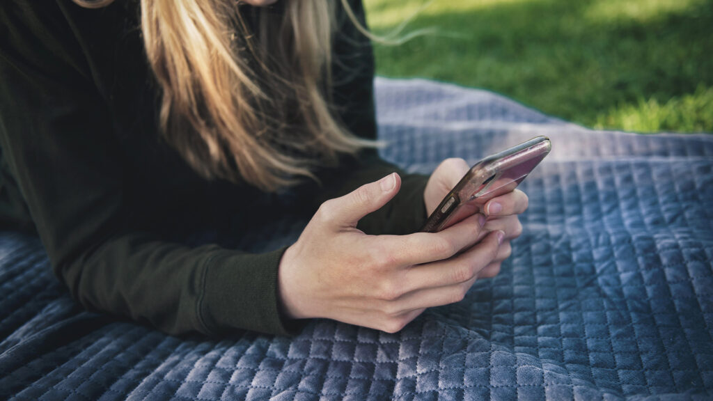 Woman holding phone on a picnic blanket